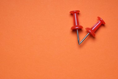 İki kırmızı raptiye koyu turuncu bir zemin üzerine yerleştiriliyor..