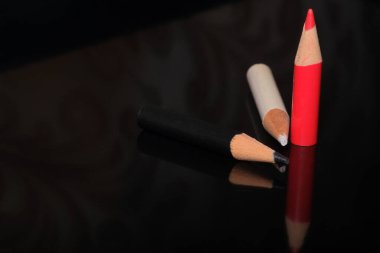 Üç renkli kalem, kırmızı, siyah ve beyaz, parlak bir yüzeye uzanır, yumuşak gölgeler bırakır..
