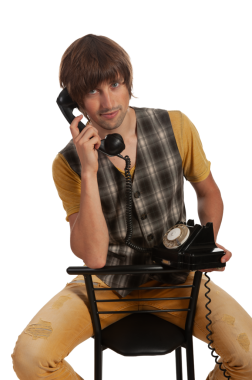 Klasik giyinmiş genç bir adam klasik bir telefonla poz veriyor, neşeli bir şekilde gülümsüyor..