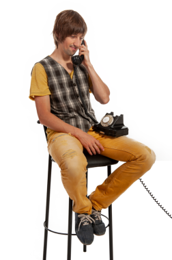 Sıradan giyimli genç bir adam klasik bir telefondan konuşurken bir taburede oturur..