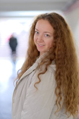 Kıvırcık saçlı kadın koridorda güvenle dikiliyor.