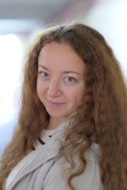 Kıvırcık saçlı genç bir kadın koridorda duruyor. Huzur ve soğukkanlılıkla.