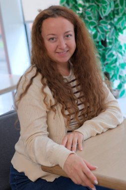 Kıvırcık saçlı bir kadın masada oturuyor, sıcak giyinmiş, huzurlu bir anın tadını çıkarıyor..