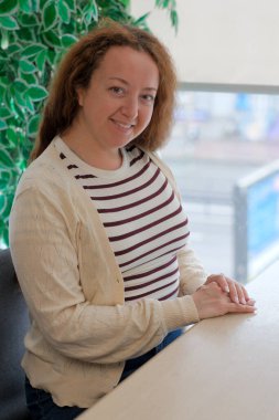 Kıvırcık saçlı bir kadın pencere kenarında oturur, çevreyle meşgul olur..