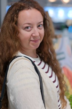 Kıvırcık saçlı bir kadın canlı piyasa tezgahlarını keşfederken nazikçe gülümsüyor..