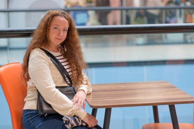 Kıvırcık saçlı bir kadın şık bir kafede dinleniyor ve huzurlu anının tadını çıkarıyor..