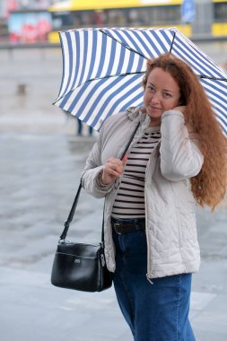 Kıvırcık saçlı kadın elinde şık bir şemsiyeyle hafif bir çiselemeyi sever..