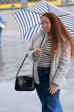 Yağmurlu bir günde, çizgili şemsiyesiyle dikkatleri üzerine çeken bir kadın..