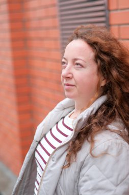 Tuğladan örülü bir duvarın yanında, gün ışığında güneşlenen bir kadın..