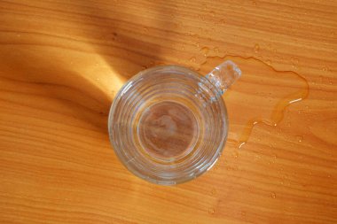 Temiz bir cam bardak pürüzsüz bir ahşap masanın üzerinde duruyor, ışığı güzel bir şekilde yakalıyor..