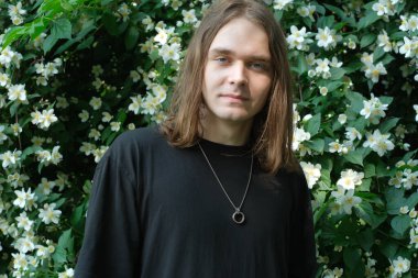 Genç bir adam canlı beyaz çiçeklerin arasında huzur içinde duruyor, doğanın güzelliğinin tadını çıkarıyor..