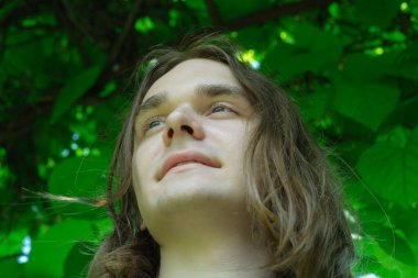 Genç bir insan yukarı bakar, canlı yaprakların altında huzur içinde yatar..