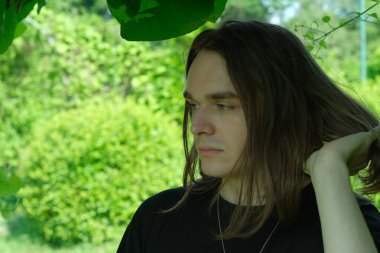 Genç bir adam düşünceli bir şekilde canlı bir yeşilliğin ortasında duruyor..