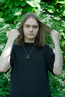 Bir insan canlı yeşilliğin ortasında duruyor, saçlarıyla oynuyor..