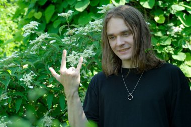 Yeşilliğin ortasında, genç bir adam neşe ve enerji dolu bir el hareketi yapıyor..