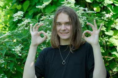 Neşeli bir genç, canlı yeşil yapraklar arasında el işaretleriyle poz verir..