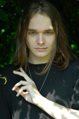 Genç bir adam yemyeşil bir ortamda, sakin bir ifadeyle güvenle duruyor..