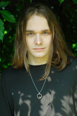 Serin, genç bir yetişkin yemyeşil bir ortamda duruyor, sakin bir güven yayıyor..