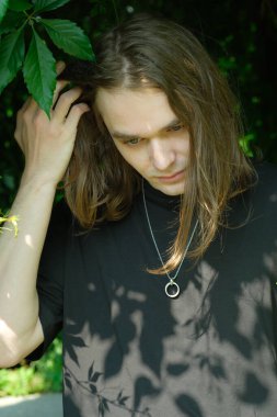 Genç bir adam yapraklı dalların altında duruyor. Düşünce ve huzur içinde kaybolmuş..