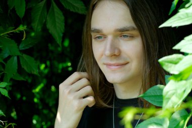 Uzun saçlı genç bir adam, canlı yapraklarla çevrili huzurlu bir anın tadını çıkarır..