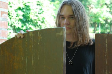 Meraklı bir birey yıpranmış bir kapının önünde duruyor, gözler canlı yeşillikte..