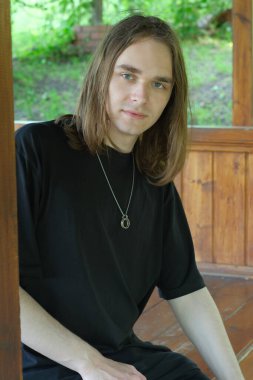 Genç bir adam yemyeşil ile çevrili ahşap bir yapıya yaslanıyor..