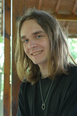 Uzun saçlı genç adam doğal ortamda dinlenirken sıcacık gülümsüyor..