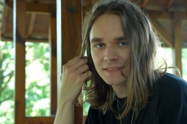 Uzun saçlı genç bir adam doğadaki ahşap bir yapıda rahatlar..