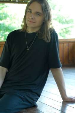 Uzun saçlı bir genç yerde öylesine oturuyor ve sakin atmosferin tadını çıkarıyor..