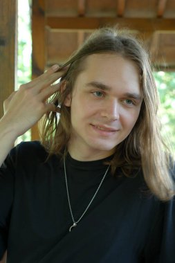 Kırsal bir alanda gülümseyen genç bir yetişkin saçlarına hafifçe dokunur..