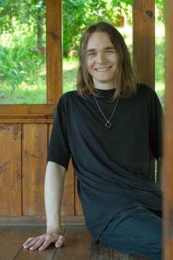 Neşeli bir genç adam kırsal bir çardakta rahatça oturur ve doğanın güzelliğinin tadını çıkarır..