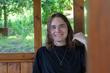 Genç bir adam ahşap bir çardakta dinleniyor, doğanın tadını çıkarırken huzur içinde gülümsüyor..