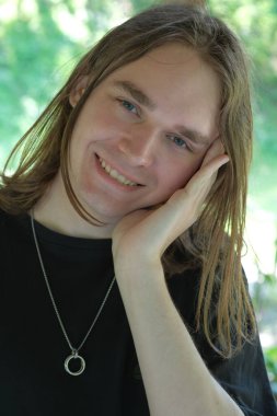 Genç bir adam nazikçe gülümser, tasasız ruhunu doğada gösterir..