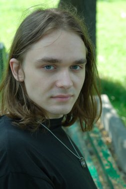 Uzun saçlı genç bir adam parktaki bankta otururken düşünceli bir şekilde bakıyor..