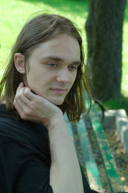 Uzun saçlı genç bir adam bir bankta oturur, düşüncelerinde kaybolur, doğayla iç içe..