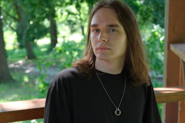 Genç bir adam, canlı yeşilliklerle çevrili ahşap bir güvertede sakince duruyor..