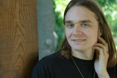 Uzun saçlı, kendinden emin genç bir adam ahşap yapının yanında, sıcaklığını yayıyor..