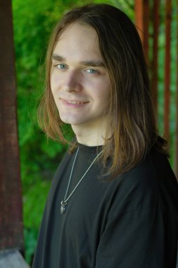 Uzun saçlı, gür yeşilliklerle çevrili neşeli genç bir adamın portresi..