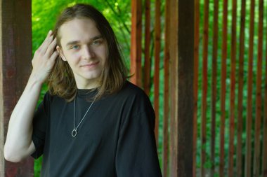 Genç bir adam canlı yeşil bir zemin üzerinde duruyor, saçlarına nazikçe dokunuyor..