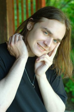 Genç bir adam açık havada, yemyeşil bir ortamda büyüleyici bir gülümseme sergiliyor..