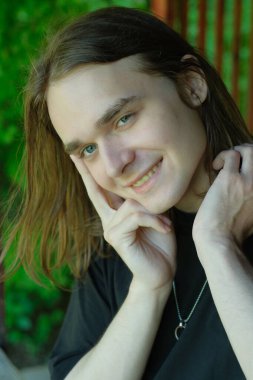 Uzun saçlı neşeli genç bir adam bahçenin güzelliğinin tadını çıkarıyor, mutluluk saçıyor..