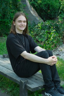 Genç bir adam, huzurlu bir parktaki yemyeşil yemyeşil bir bankta dinleniyor..