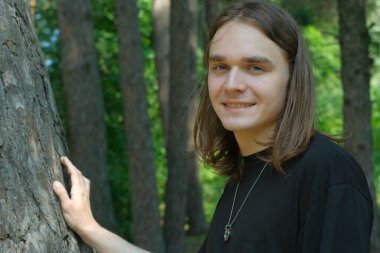 Genç bir adam, yükselen yeşil ağaçların arasında gülümseyen yaşlı bir ağaca karşı duruyor..