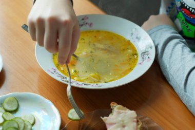 Bir el sıcak bir kase çorbanın yanında taze salatalık dilimleri için uzanır..