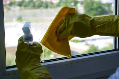 Parlak güneş ışığı ellerde parlıyor. Eldivenlerle pencereyi özenle temizliyor..