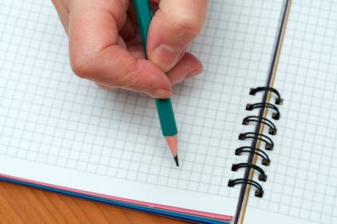 Bir insan eli kalemi kavrayıp boş bir kılavuz defteri üzerinde fikirler yaratmaya hazırlanıyor.