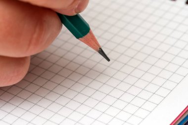 Yeşil kalemi tutan bir el kare kağıda fikirler yazmaya hazırlanır..