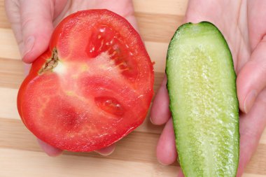 Bir insan elinde parlak bir domates ve kıtır kıtır bir salatalık tutar..