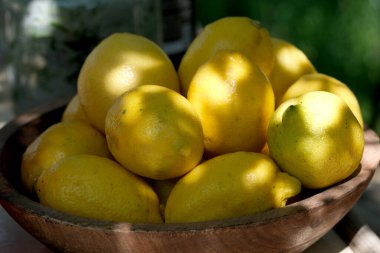 Parlak sarı limonlar, yumuşak güneş ışığı altında, ahşap bir kasede dinleniyor, tazelik yayıyorlar..