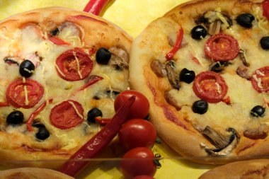 Çok güzel hazırlanmış iki pizza canlı bir arka planda bir dizi taze malzeme sergiliyor..